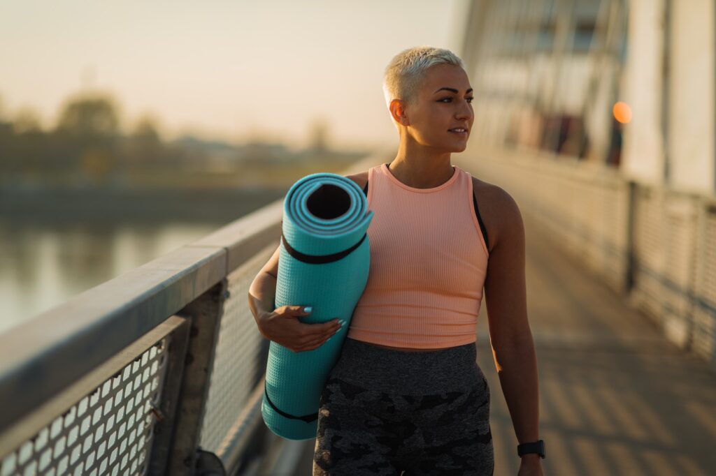 Young woman carrying exercise mat and crossing bridge